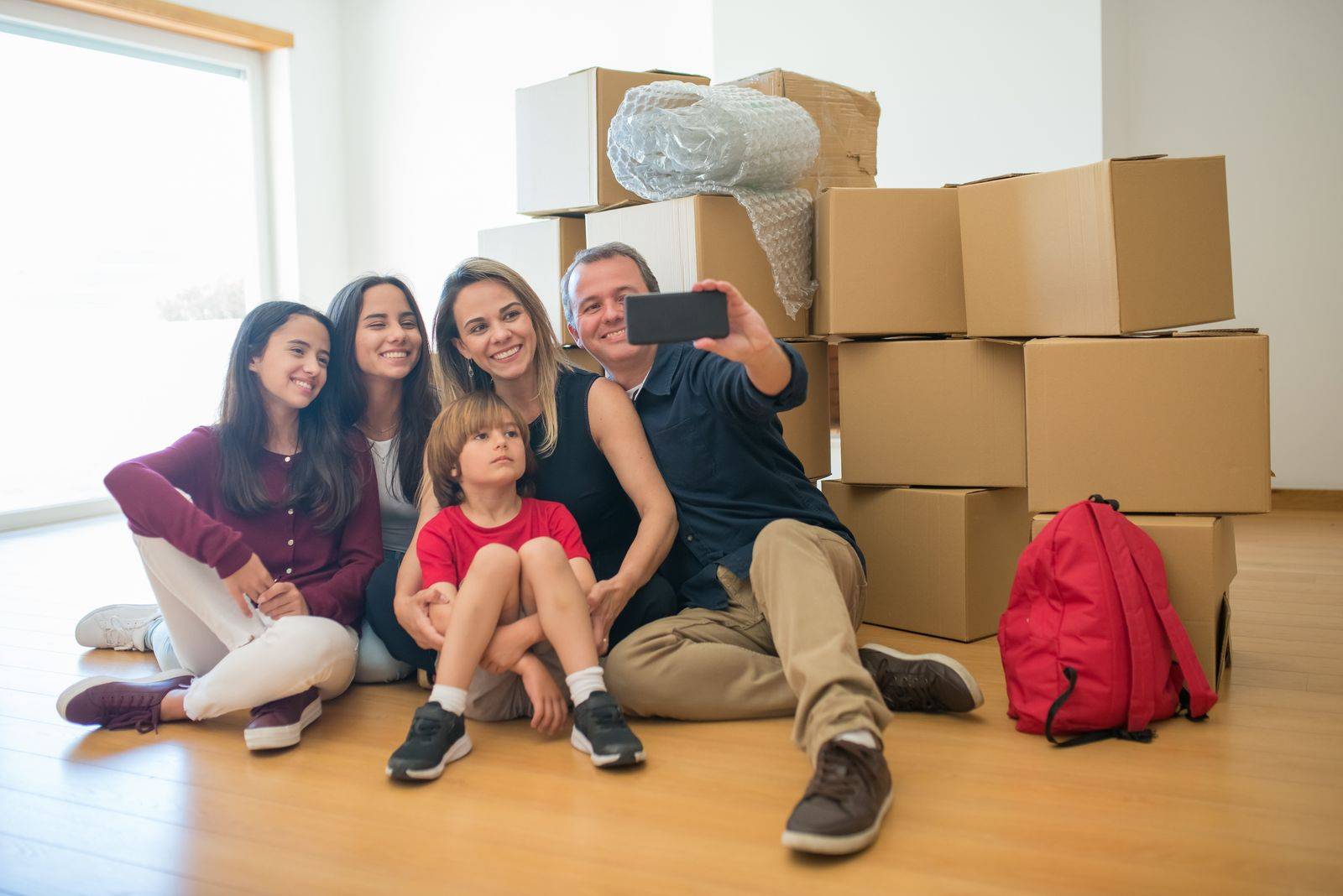 Família sentada no chão de um apartamento novo, entre caixas de mudança