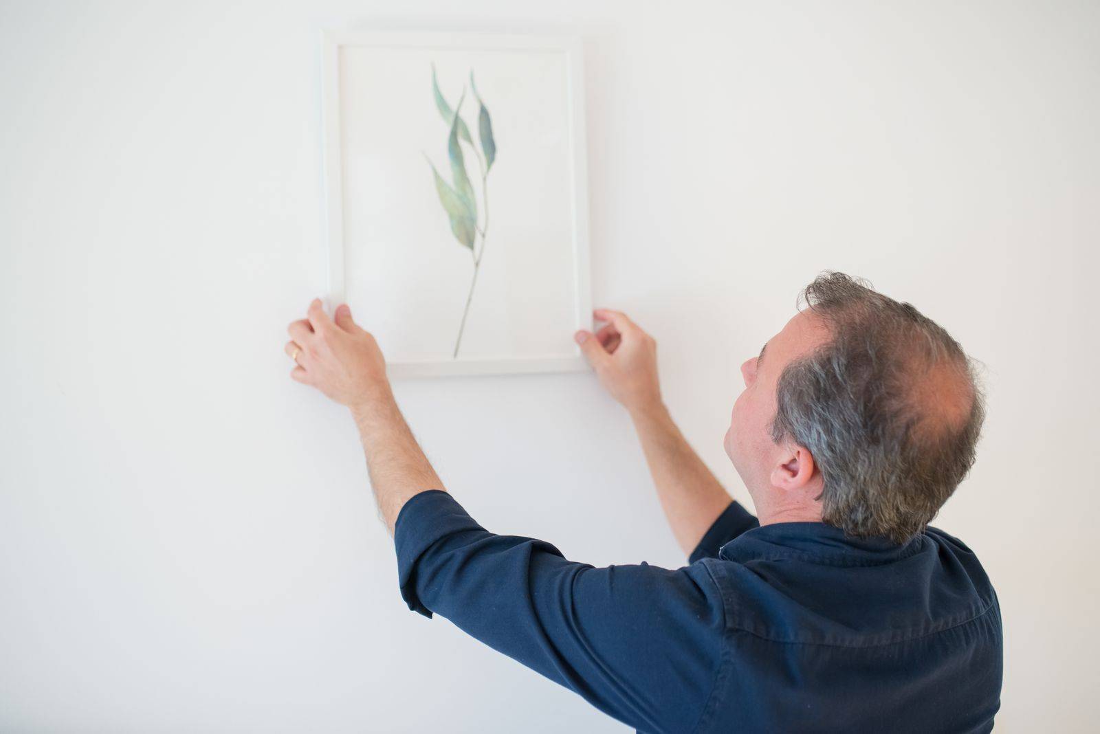 Morador pendurando um quadro na parede da casa nova